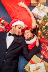 Ein Paar mit Weihnachtsmützen liegt auf dem Boden zwischen Geschenken