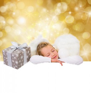 Kind im Engelskostüm schlafend neben einem Geschenk