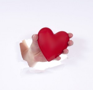 Eine Hand die durch ein Loch ein rotes Herz hält