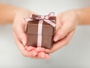 braunes Geschenk mit rosa Schleife wird in 2 Händen gehalten