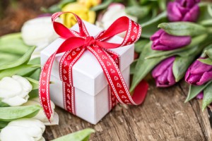 weißes Geschenk mit roter Schleife auf Holz mit bunten Blumen