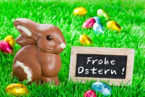 Schoko Osterhase auf einer Wiese und einem Schild mit der Aufschrift Frohe Ostern