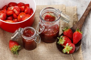 Zwei offene Einmachgläser mit Erdbeerkonfitüre auf ein Tisch mit frischen Erdbeeren