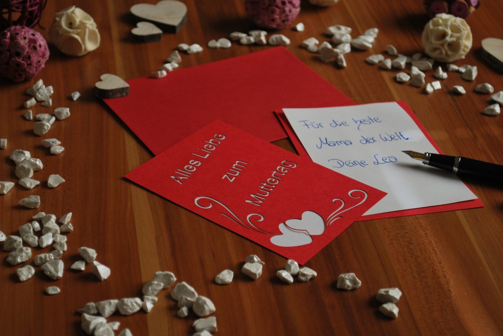 Rote selbstgestaltete Muttertagskarte mit rotem Umschlag, Füller und passende Dekoration.