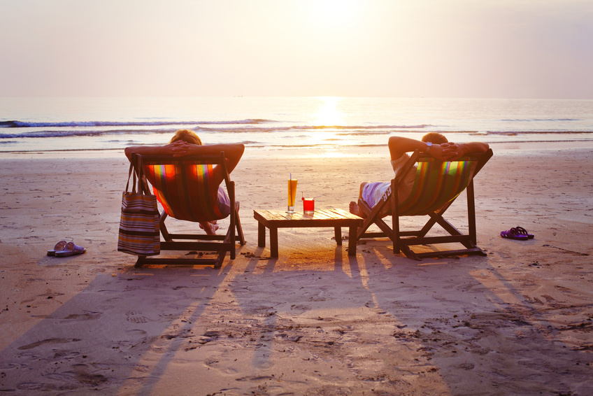Zwei MEnschen genießen den Sonnenuntergang am Strand auf einer Liege.