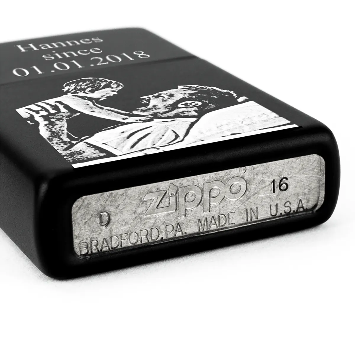 schwarzes Zippo mit Foto und Text graviert auf dem Boden liegend mit Stempel Unterseite sichtbar